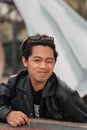 an Asian man with a chubby face wearing sunglasses and a black leather jacket while sitting at a cafe table Royalty Free Stock Photo