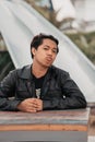 an Asian man with a chubby face wearing sunglasses and a black leather jacket while sitting at a cafe table Royalty Free Stock Photo