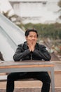 an Asian man with a chubby face wearing sunglasses and a black leather jacket while sitting at a cafe table Royalty Free Stock Photo