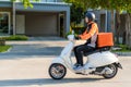 Asian man courier on scooter delivering food in town streets with a hot food delivery from take aways and restaurants to home,