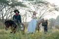 Asian man with cowboy costume stay on horse with take care pretty woman with white dress on horse look like he guard or protect