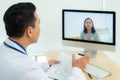 Asian man doctor wears white coat and headset speaking videoconferencing on laptop computer using online video call consultation