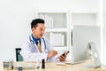 Asian man doctor wears white coat and headset speaking videoconferencing on laptop computer using online video call consultation