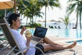 Asian man drinking coconut water while he is working on his laptop on a chairnear pool at resort hotel on summer vacation holiday Royalty Free Stock Photo