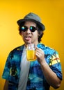 Asian Man Drinking Orange Juice Wearing Fedora Hat and Sunglasses against Yellow Background