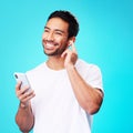 Asian man, earphones and smartphone in studio for music, podcast app and blue background. Happy male model thinking with Royalty Free Stock Photo