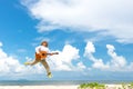 Asian man enjoying summer, playing classic guitar and jumping on the beach in vacations, blue sky background