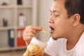 Asian man enjoys eating casava or potato chips while sitting on sofa at living room Royalty Free Stock Photo