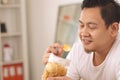 Asian man enjoys eating casava or potato chips while sitting on sofa at living room Royalty Free Stock Photo