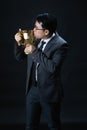 Asian man in formal suit kissing trophy