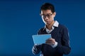 Glasses-clad man engrossed in tablet, blue backdrop