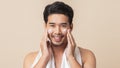 Asian man happy smiling and applying moisturizer skin care cream on face after take a shower on brown background