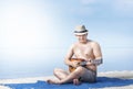 Asian man in hat sitting and playing guitar on the carpet in beach Royalty Free Stock Photo