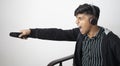 Asian man with headphone wearing black jacket holding remote excited to the match with arms raised and open eyes