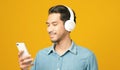 Asian man with headphones holding mobile phone smiling while listening to music isolated on yellow background, People and Royalty Free Stock Photo