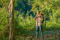 Asian man with hiking accessories and backpack walk along the way in forest and stop with hold binoculars look like he find