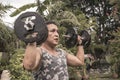 A asian man in his early 50s does standing dumbbell shoulder presses at his front yard. Fitness and working out at home