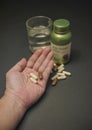 Asian man holding many pills on hand with a glass of water and a bottle of vitamin on a black background.