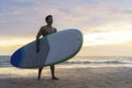 Asian man holding a sup board and paddle and walking on the beach. In the background, the ocean and the sunset. Back view. Summer Royalty Free Stock Photo