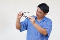 Asian man holds his eyeglasses to check because it not adjust focus with his eyesight.