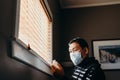 Asian man in isolation looking at medicine bottle. Man in medical mask forced to stay inside the house as a result of the