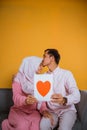 Asian man kisses hijab woman showing a paper love drawing