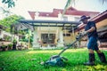 Asian man mowing lawn in the garden with blurry house. Mowing or cutting the long grass with electric lawn mower Royalty Free Stock Photo