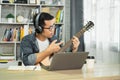 Asian man musicians wearing headphone and learning guitar online via video, mastering skills, while teaching students with passion