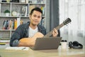 Asian man musicians wearing headphone and learning guitar online via video, mastering skills, while teaching students with passion