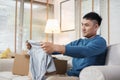 Asian man open cardboard boxes  while moving to new home at sofa in living room.unpacking for new house Royalty Free Stock Photo