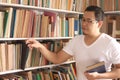 Asian man picking book in bookshelf, education concept, reading learning studying in library, happy smiling Royalty Free Stock Photo