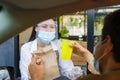 Asian man in protective mask taking food bag and coffee with woman waitress wearing face mask and face shield at drive thru during Royalty Free Stock Photo
