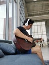 Asian business man with headset sitting on couch and playing guitar fish for