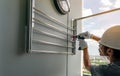 Asian man screwing screw install clothesline with cordless drill. Technician wears safety helmet and hand holding drilling tool