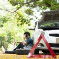 Asian man sitting beside car and using mobile phone calling for assistance after a car breakdown on street. Concept of vehicle Royalty Free Stock Photo