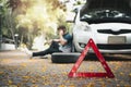 Asian man sitting beside car and using mobile phone calling for assistance after a car breakdown on street. Concept of vehicle Royalty Free Stock Photo