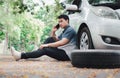 Asian man sitting beside car and using mobile phone calling for assistance after a car breakdown on street. Concept of vehicle Royalty Free Stock Photo