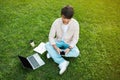 Asian man sitting on grass while using phone and laptop Royalty Free Stock Photo