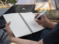 An Asian man sitting is holding a pen writing note of letter memorize memories on book in outside the tent