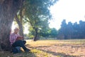 Asian man sitting under big tree and reading book.he is reading book and relaxing time in public park.