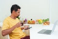 Asian man sitting working in at home, there is laptop computer on table, sat play phone after long hours work breaks, sit back Royalty Free Stock Photo