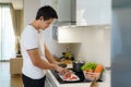 An Asian man slices tomatoes on a kitchen counter to prepare for dinner at home