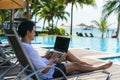 Asian man spent his summer vacation working on his laptop in a chair near the swimming pool in resort hotel near sea Royalty Free Stock Photo