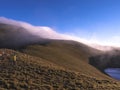 An asian man standing on the hill of mountains, and there is a thick fog drifting torward where he is