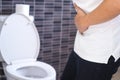 An Asian man stands near a toilet bowl. Have a stomachache, constipation in the bathroom. The handle on the stomach is sick due to