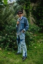 an Asian man in sunglasses and a denim shirt standing in front of a flowering plant Royalty Free Stock Photo