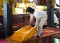 Asian Man supports and prepares orange monk seat on the red carpet in wood pavilion temple