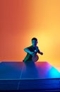 Asian man, table tennis player poised to strike in neon light against warm yellow gradient background. Dynamic gel