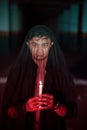an Asian man with a transparent hood covered in blood holds a candle in his hand with a very scary expression