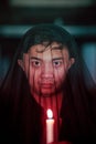 an Asian man with a transparent hood covered in blood holds a candle in his hand with a very scary expression